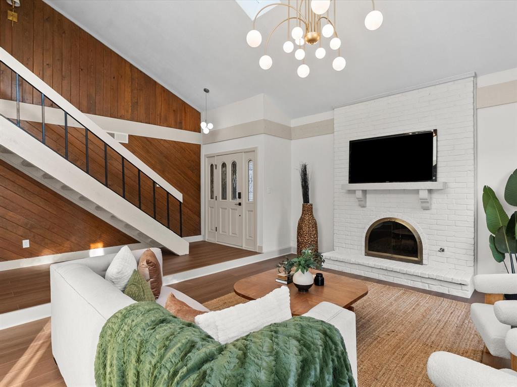 Vaulted ceilings featuring a skylight, floor-to-ceiling wood paneled accent wall, whitewashed brick fireplace, and modern multi-globe chandelier