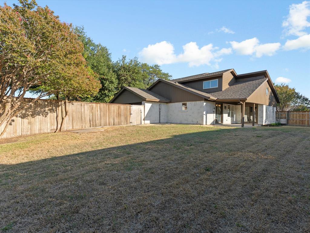 Expansive backyard featuring a stone and siding exterior, a covered patio, mature trees, and a full-perimeter wood fence