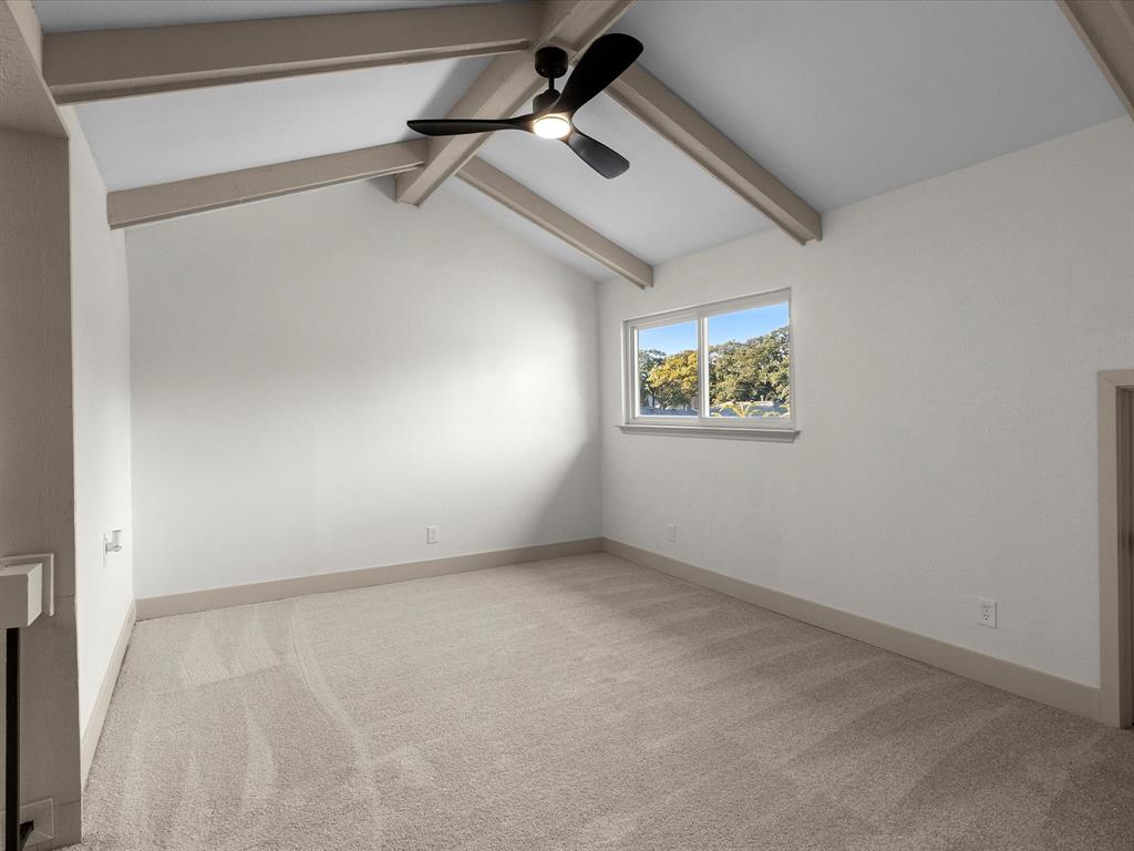 Vaulted ceiling featuring exposed beams, carpeted flooring, and a modern ceiling fan