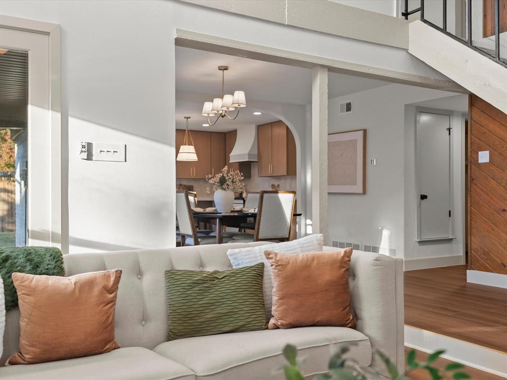 Arched entryway featuring a neutral color palette, wood-finish flooring, vertical wood plank wall paneling, multi-arm chandelier lighting, and a staircase with metal railings