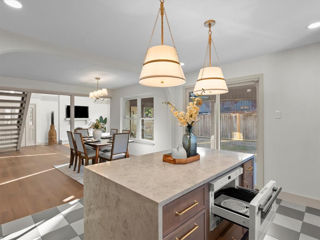 Center island featuring stone-finish countertop, built-in microwave drawer, and wood-finish cabinetry with brass-tone hardware, accented by dual pendant lights