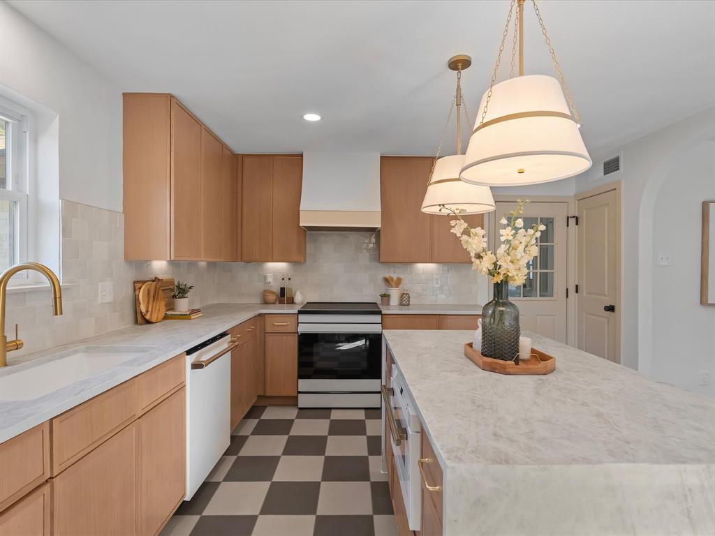 Kitchen featuring light wood-finish cabinetry, a central island with a stone countertop, a brass faucet, a custom range hood, and a checkerboard pattern tile floor