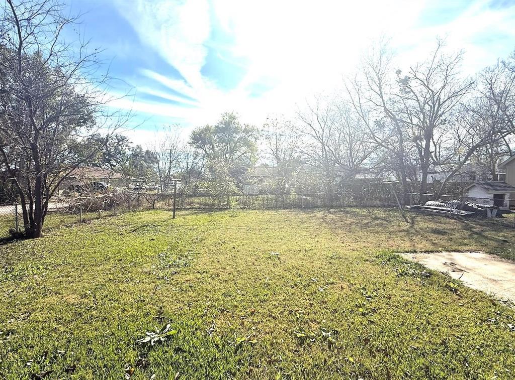 Open backyard featuring a chain-link perimeter fence, concrete slab, and mature trees
