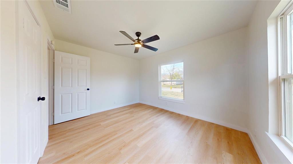 Neutral-toned room featuring wood-finish flooring, a ceiling fan with integrated lighting, dual-panel interior doors, and multiple windows