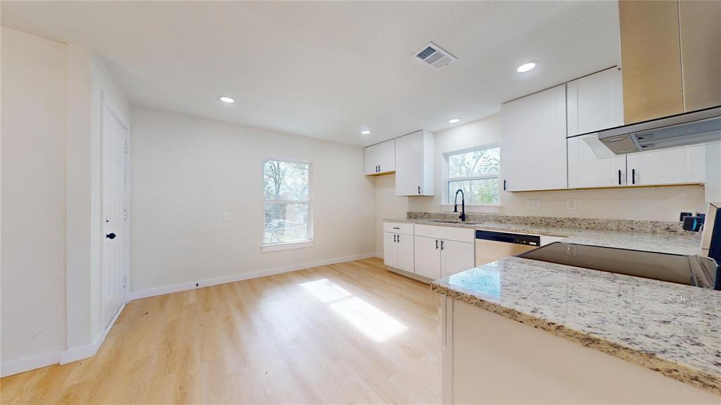 Kitchen featuring white shaker-style cabinetry, stone countertops, integrated stainless steel appliances, a matte black faucet, and wood-finish flooring