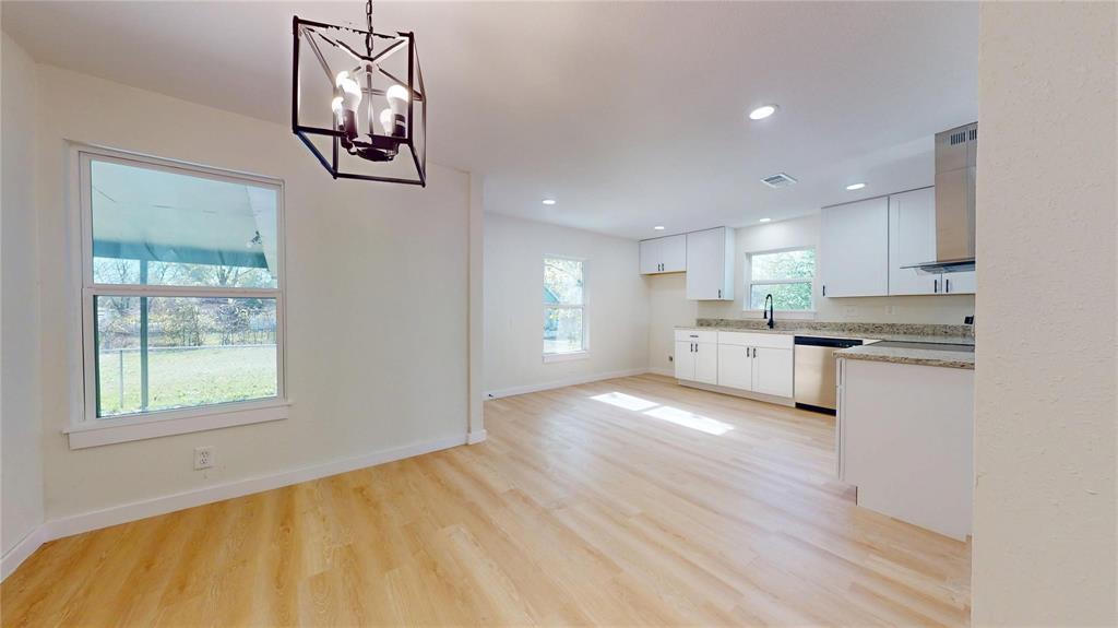 Open-concept area featuring wood-finish flooring, white cabinetry, stone-finish countertops, stainless steel appliances, and a geometric metal pendant light