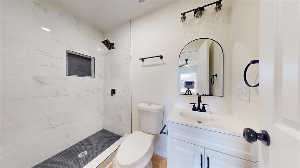 Walk-in shower with floor-to-ceiling stone-pattern tile, contrasting dark mosaic floor, built-in recessed wall niche, arched vanity mirror, and matte black hardware