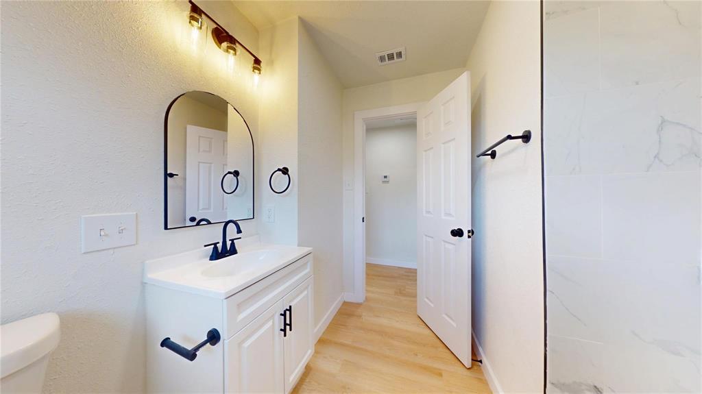 Bathroom featuring a vanity with a white cabinetry base, arched wall mirror, stone-finish shower surround, and matte black fixtures