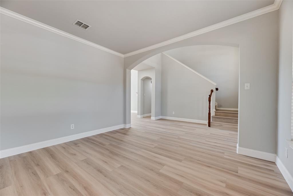 Interior space featuring wood-finish flooring, neutral wall tones, arched wall openings, crown molding, and a staircase with a dark wood handrail
