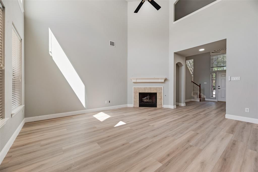 Two-story living area featuring wood-finish flooring, vaulted ceilings, a fireplace with a mantel, and a ceiling fan