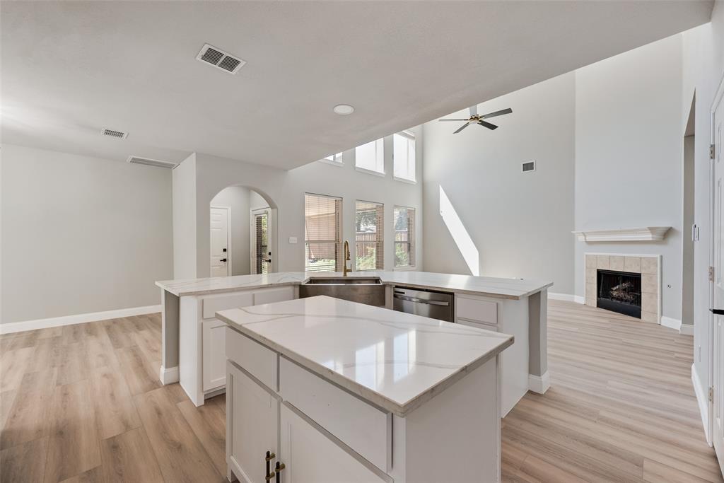 Kitchen featuring a central island with a stone-finish countertop, stainless steel undermount sink, white cabinetry, and wood-finish flooring
