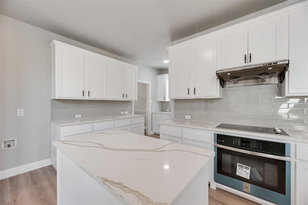 Kitchen featuring a central island with a quartz countertop, white shaker-style cabinetry, a light gray subway tile backsplash, and stainless steel appliances