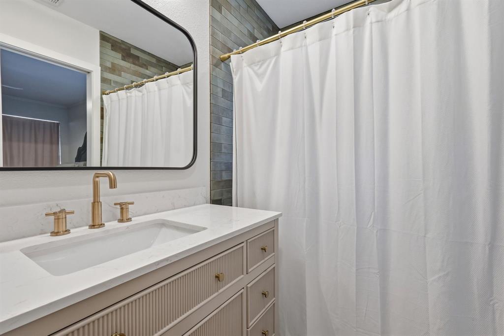 Bathroom vanity featuring a fluted cabinet base, stone-surface countertop, rectangular undermount sink, brass-finish widespread faucet, and a black-framed rectangular wall mirror