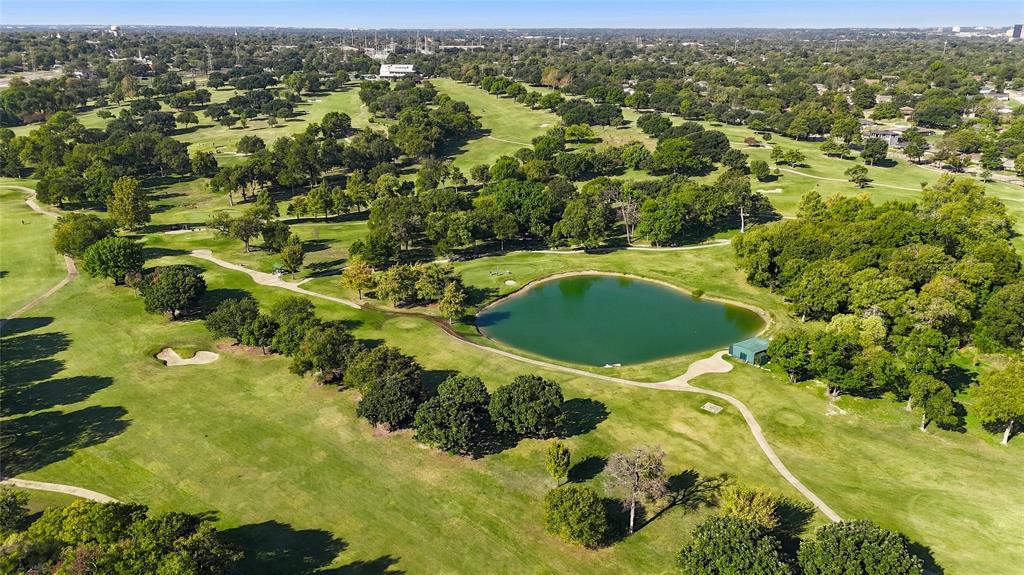 Aerial perspective of a golf course featuring expansive green fairways, mature tree canopy, a central pond, and sand bunkers