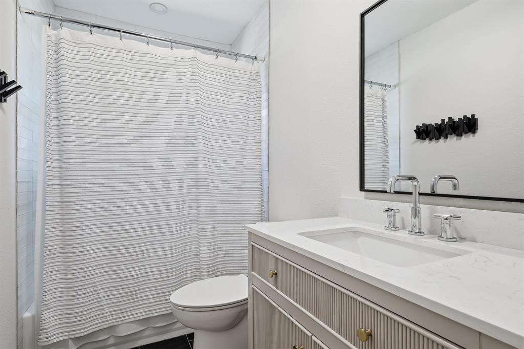 Bathroom featuring a vanity with fluted cabinetry, light-toned countertop, integrated rectangular sink, polished chrome widespread faucet, and a rectangular mirror with a black frame