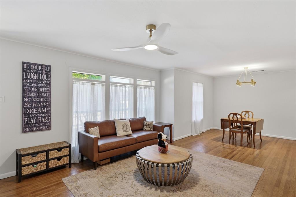 Open-concept interior featuring wood-finish flooring, triple-pane window configuration, integrated ceiling fan with light, and modern tiered chandelier