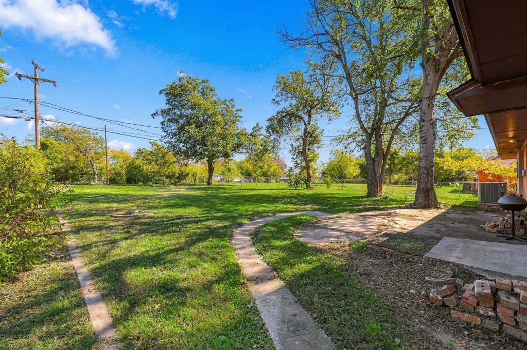 Expansive backyard featuring a concrete patio, stone pathway, mature trees, and perimeter chain-link fencing