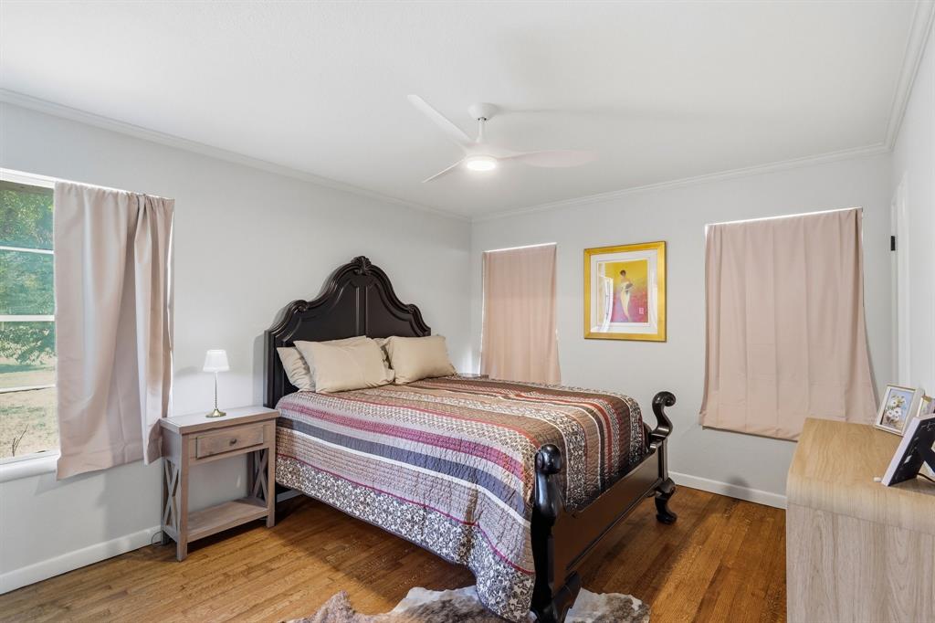 Bedroom featuring wood-finish flooring, three windows with natural light, and a white ceiling fan with integrated lighting