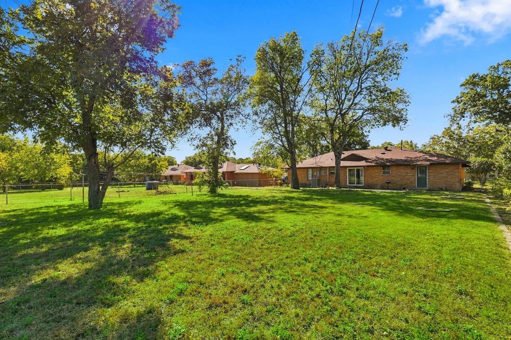 Expansive backyard featuring a brick exterior residence, mature shade trees, and a perimeter fence