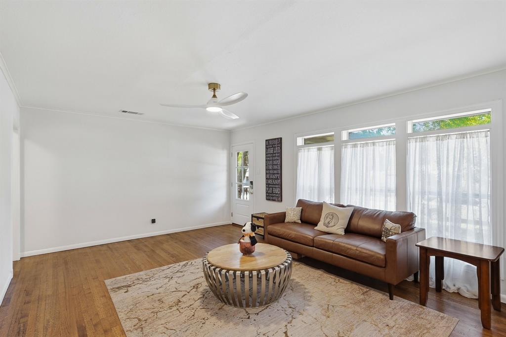 Wood-finish flooring, white walls, and a ceiling-mounted light fixture with fan blades, complemented by a series of windows
