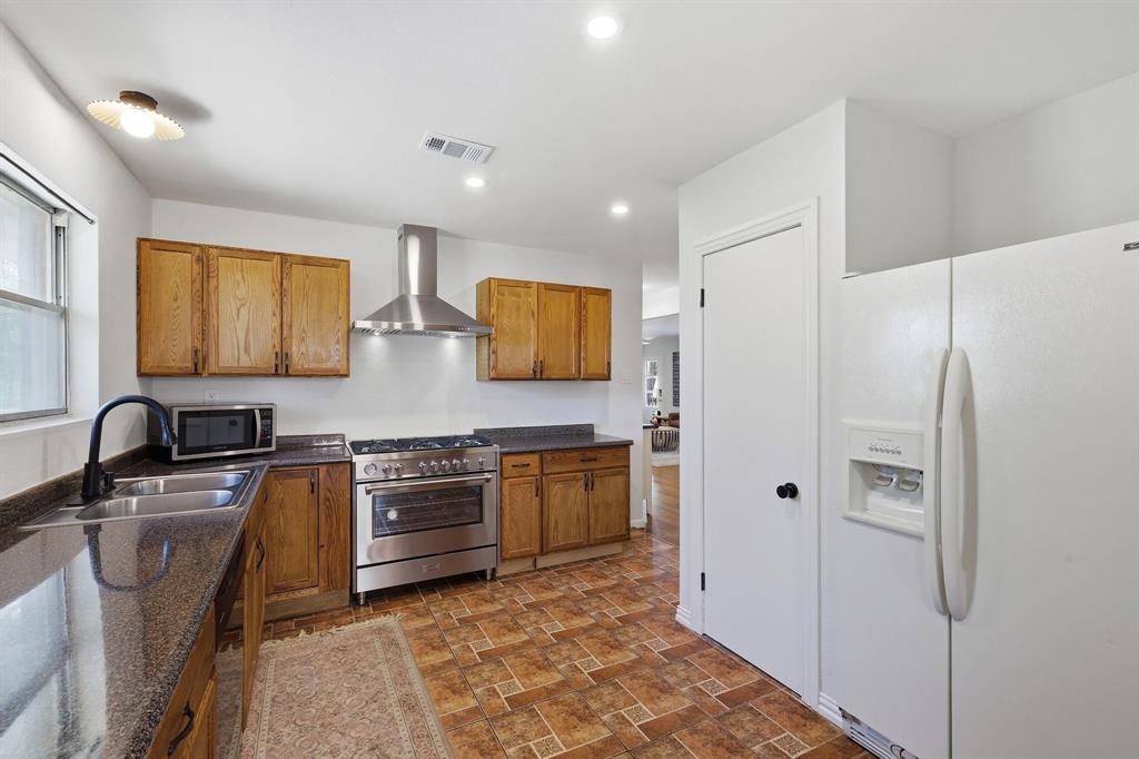 Kitchen featuring wood cabinetry, stone-surface countertops, stainless steel range with matching ventilation hood, and recessed lighting