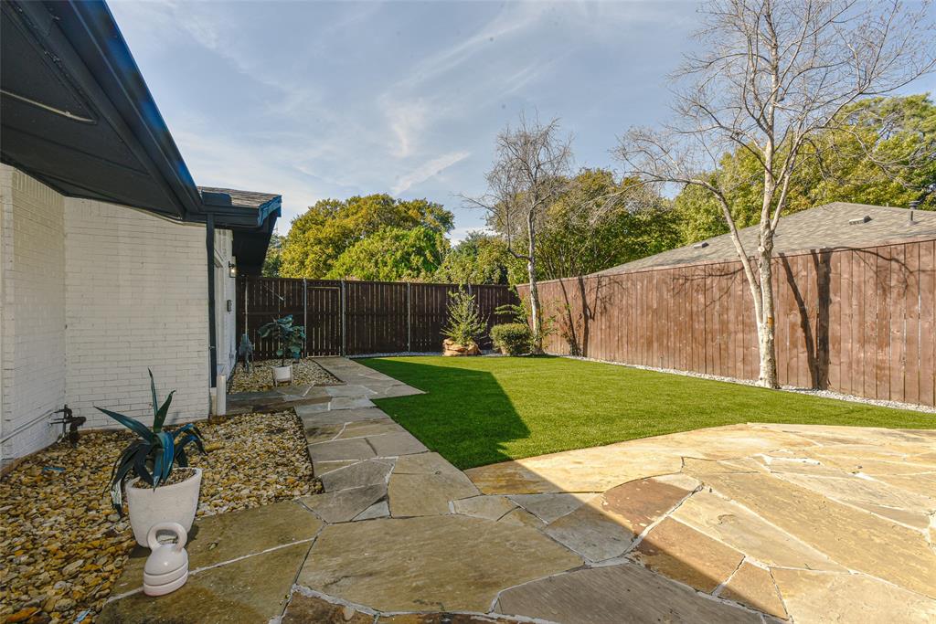 Private backyard featuring expansive flagstone patio, synthetic turf lawn, white painted brick exterior, and perimeter wood privacy fencing