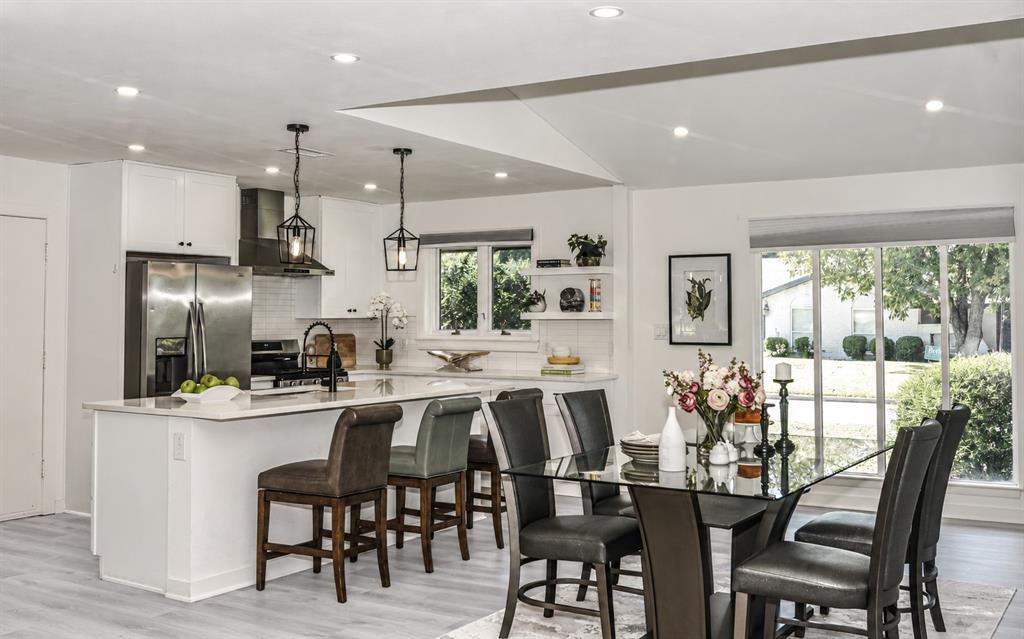 Open-concept kitchen featuring a waterfall-edge stone island, stainless steel appliances, matte black fixtures, recessed lighting, and white cabinetry Open-concept kitchen featuring a waterfall-edge stone island, stainless steel appliances, matte black fixtures, recessed lighting, and white cabinetry