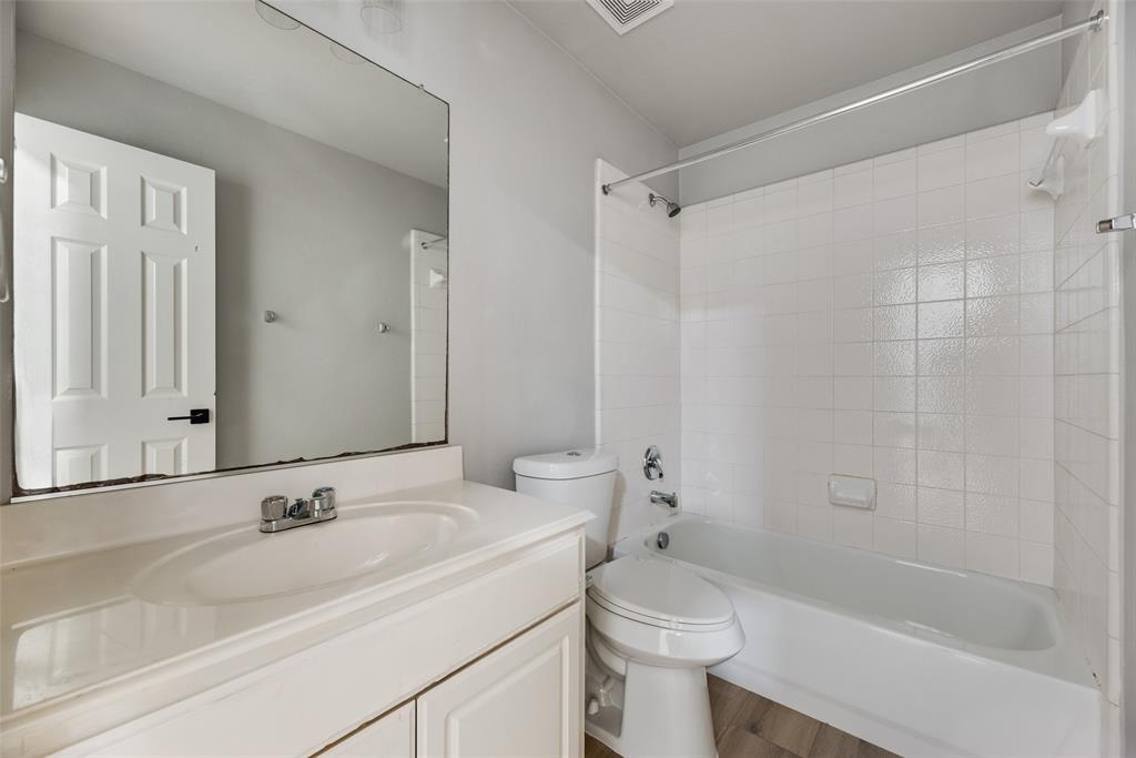 Bathroom featuring a white vanity cabinet with an integrated sink, a large wall-mounted mirror, a two-piece toilet, and a tub-shower combination with white wall tile Bathroom featuring a white vanity cabinet with an integrated sink, a large wall-mounted mirror, a two-piece toilet, and a tub-shower combination with white wall tile