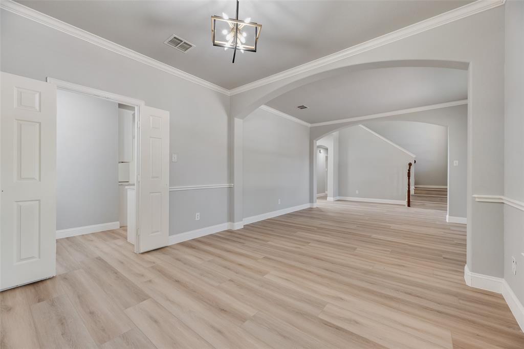Open interior featuring wood-finish flooring, architectural arched openings, crown molding, chair rail trim, and a modern geometric light fixture Open interior featuring wood-finish flooring, architectural arched openings, crown molding, chair rail trim, and a modern geometric light fixture