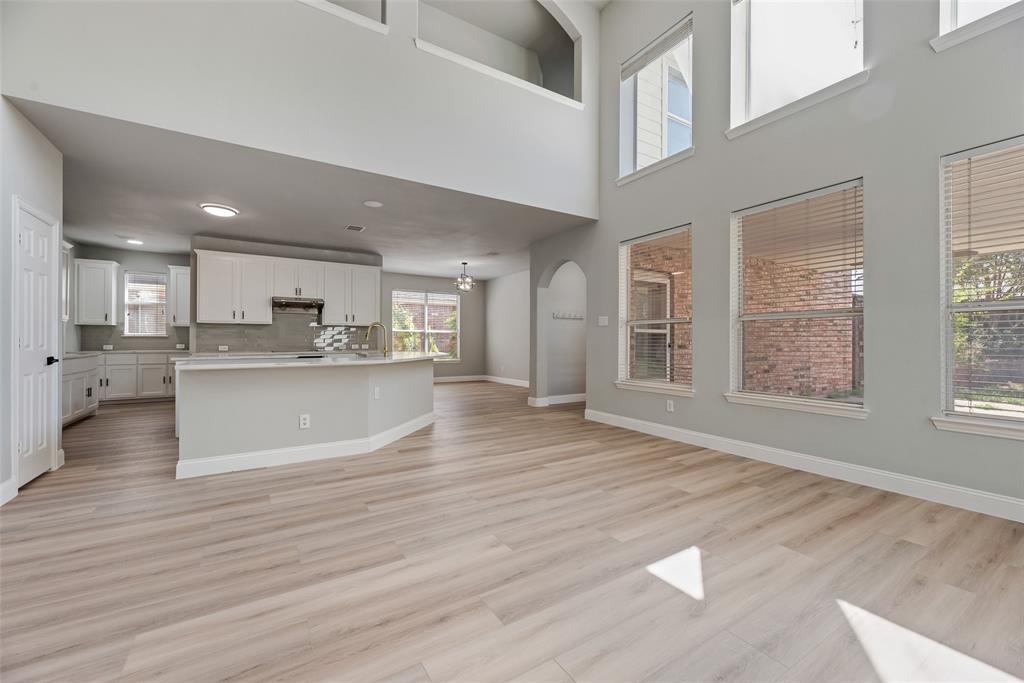 Two-story height ceiling with multi-level windows, wood-finish flooring, kitchen featuring white cabinetry and a center island, and arched architectural details