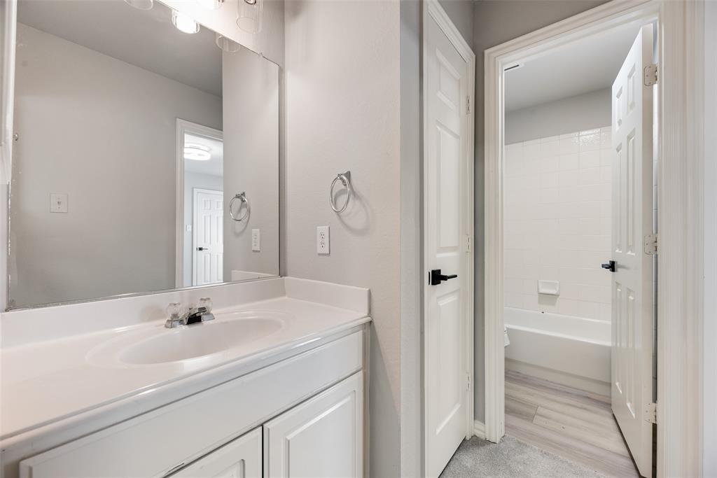 Bathroom featuring a white vanity cabinet with an integrated sink, a large wall-mounted mirror, brushed metal fixtures, and a shower-tub combination with tile surround Bathroom featuring a white vanity cabinet with an integrated sink, a large wall-mounted mirror, brushed metal fixtures, and a shower-tub combination with tile surround