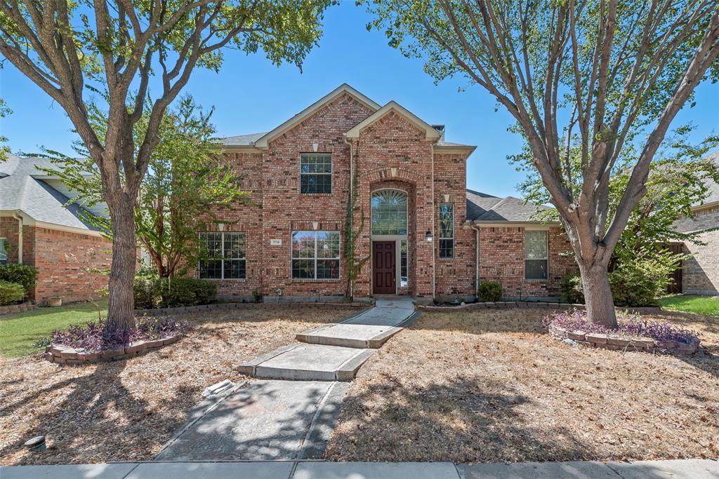Two-story brick exterior featuring an arched entryway, decorative stone-bordered landscaping, and a concrete walkway Two-story brick exterior featuring an arched entryway, decorative stone-bordered landscaping, and a concrete walkway