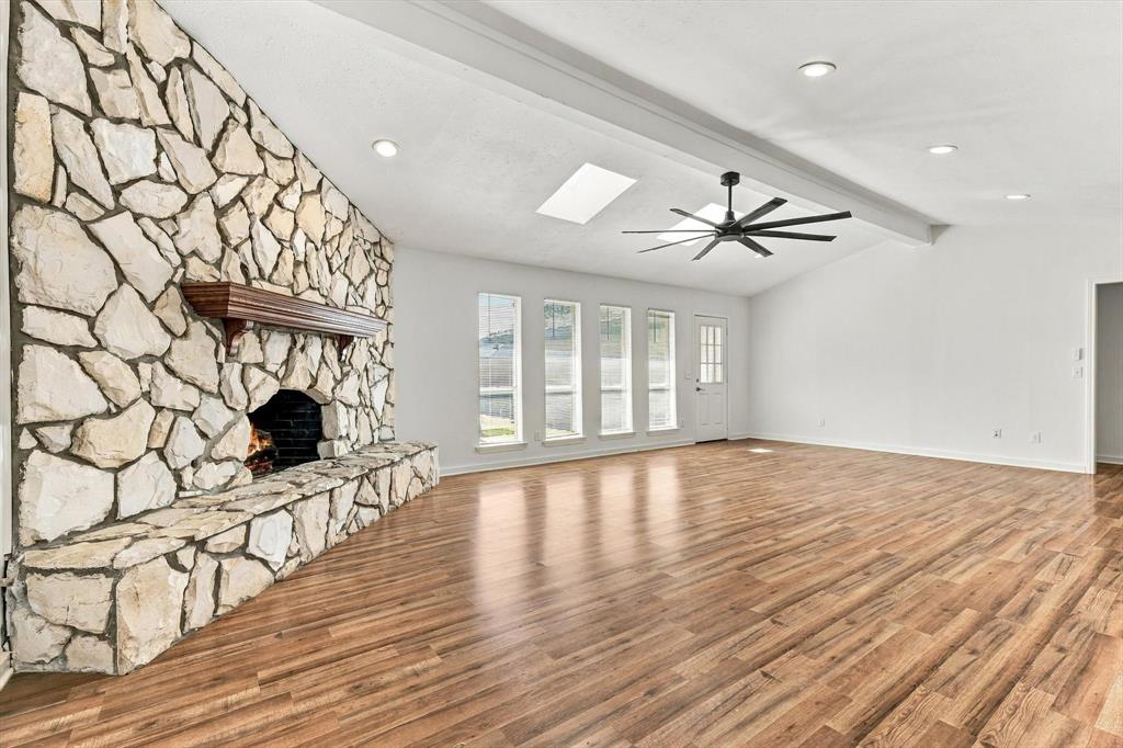 Floor-to-ceiling stone fireplace with a wood mantel, wood-finish flooring, vaulted ceiling with recessed lighting, skylights, and a multi-blade ceiling fan