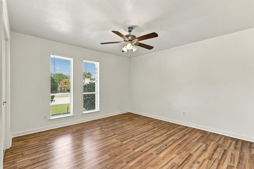 Interior room featuring wood-finish flooring, dual vertical windows, and a ceiling fan with integrated lighting