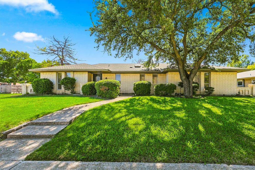 Single-story residence with a light-colored brick exterior, hip roof, concrete walkway, and mature landscaping