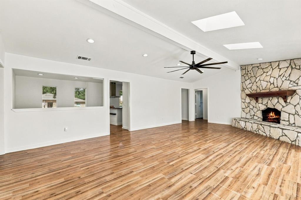 Living area featuring wood-finish flooring, floor-to-ceiling natural stone fireplace, skylights, recessed lighting, and a modern ceiling fan