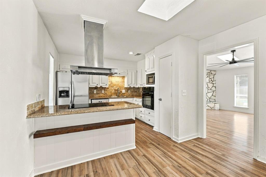 Kitchen featuring stone countertops, white cabinetry, stainless steel vent hood, wood-finish flooring, and a skylight