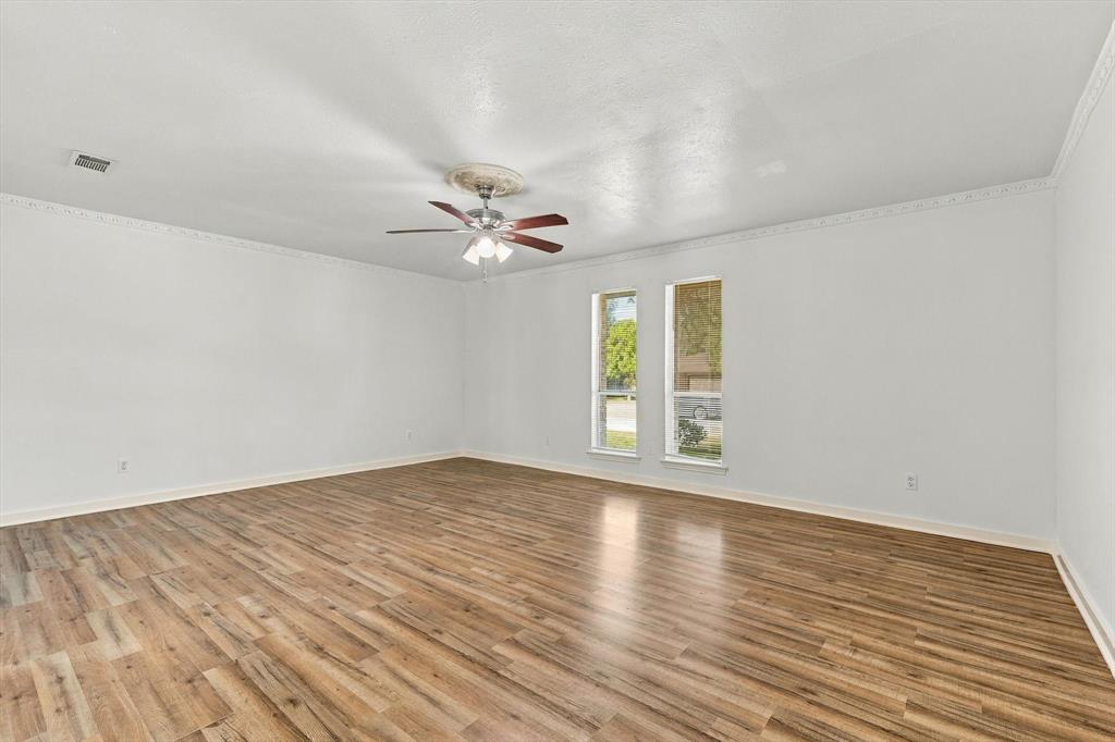 Spacious room featuring wood-finish flooring, crown molding, dual windows, and a central ceiling fan with integrated light fixture