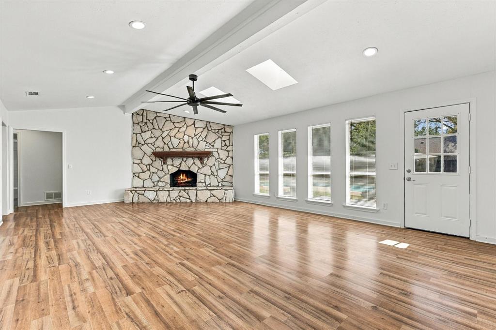 Spacious room featuring wood-finish flooring, a floor-to-ceiling stone fireplace, skylights, recessed lighting, and a multi-blade ceiling fan