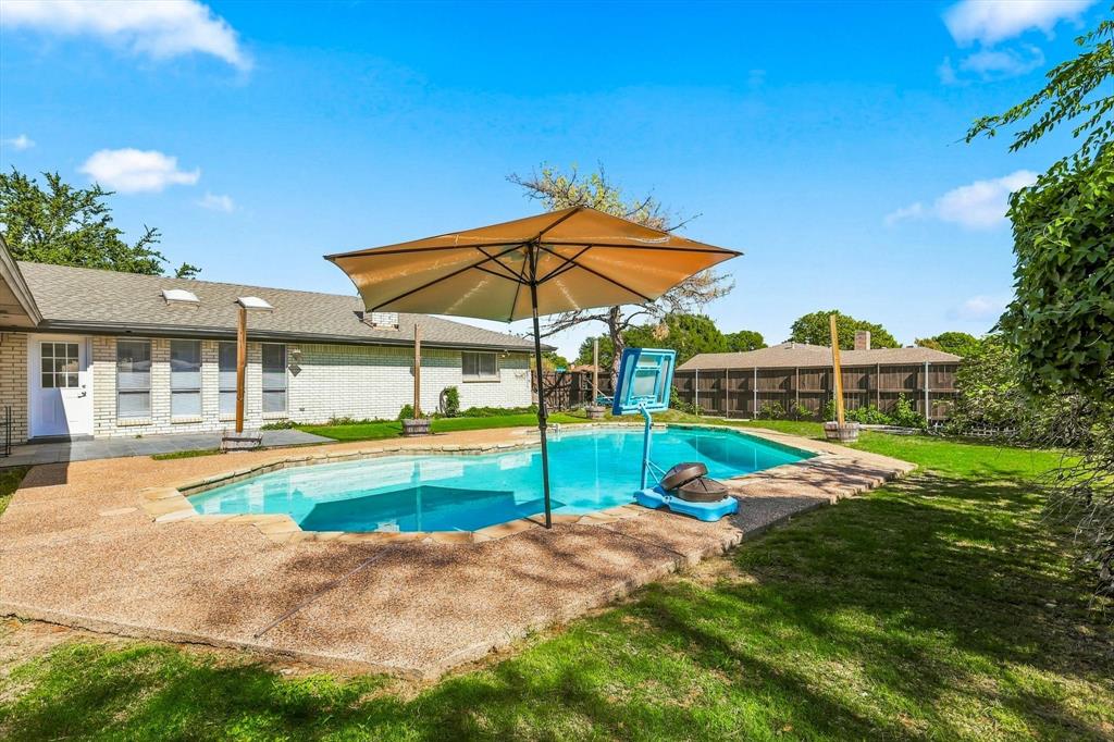In-ground swimming pool with a concrete surround, brick exterior, skylights, and wood-fence perimeter