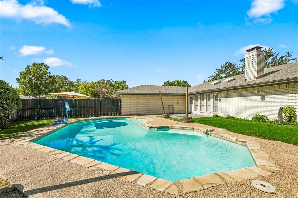 Backyard featuring an in-ground swimming pool, flagstone coping, aggregate concrete decking, perimeter wood fencing, and brick exterior walls