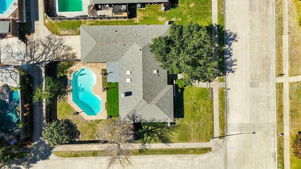 Aerial perspective featuring a corner lot, a swimming pool with a concrete deck, a composition shingle roof, and mature trees