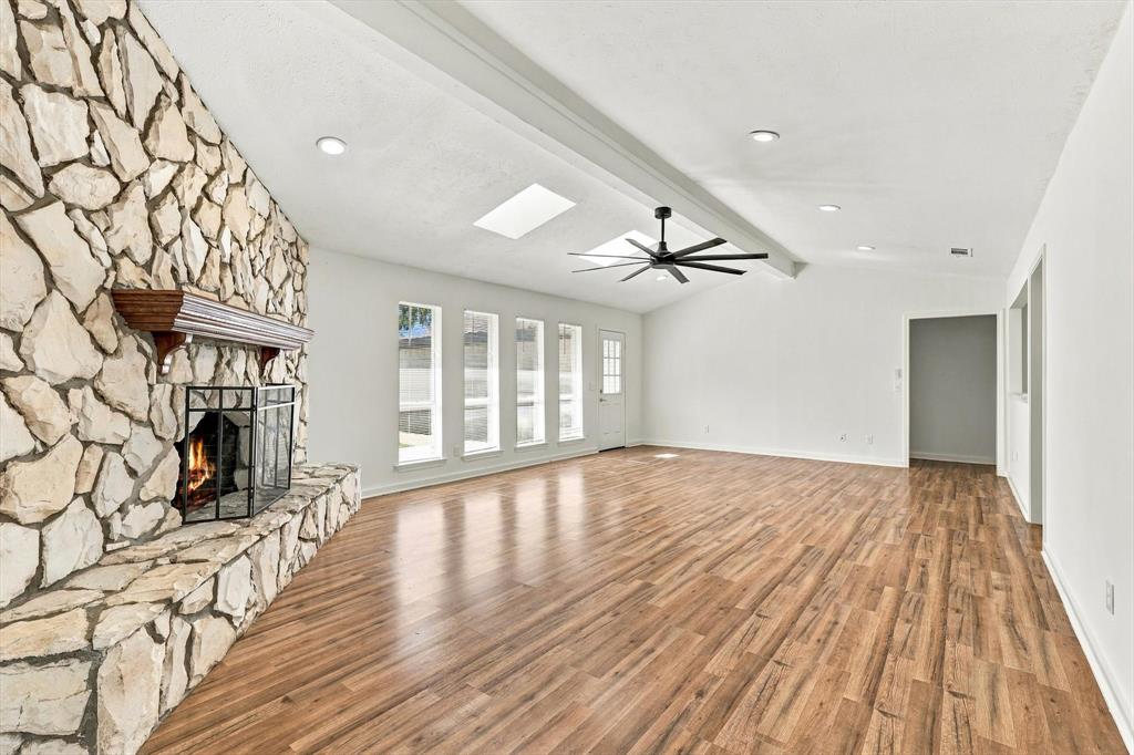 Full-height floor-to-ceiling stone fireplace with a prominent wooden mantel, wood-finish flooring, recessed lighting, dual skylights, and a ceiling fan