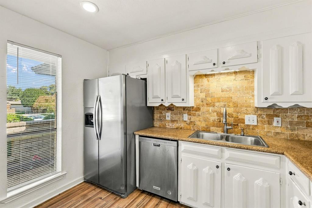 Kitchen featuring white cabinetry, stainless steel appliances, natural stone tile backsplash, wood-finish flooring, and recessed lighting