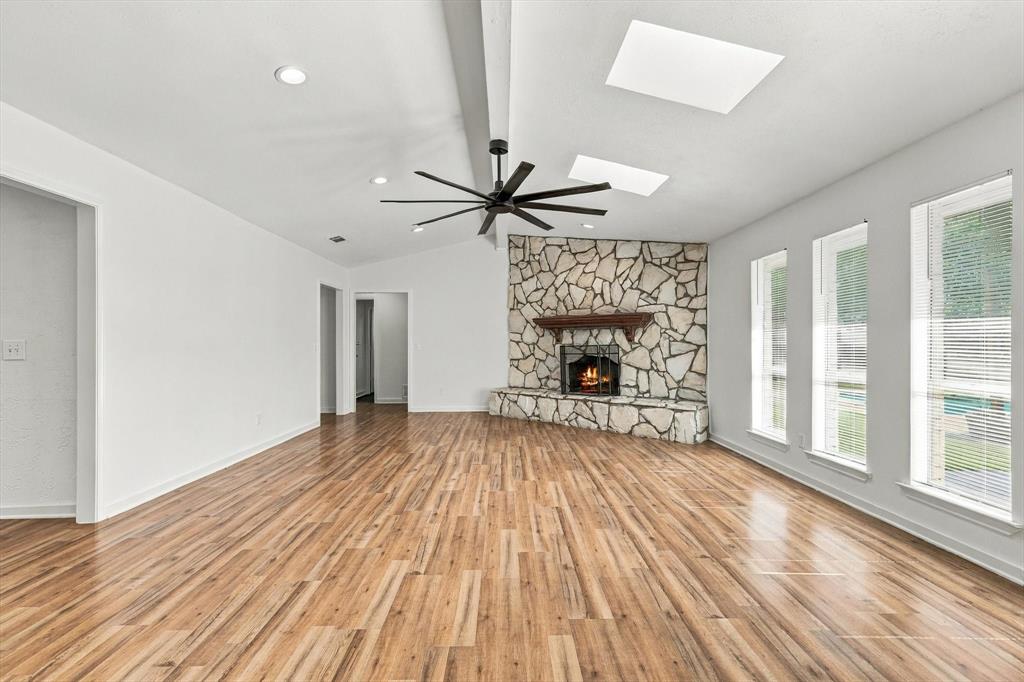 Vaulted ceiling with skylights, wood-finish flooring, full-height stone-clad fireplace, and large multi-pane windows