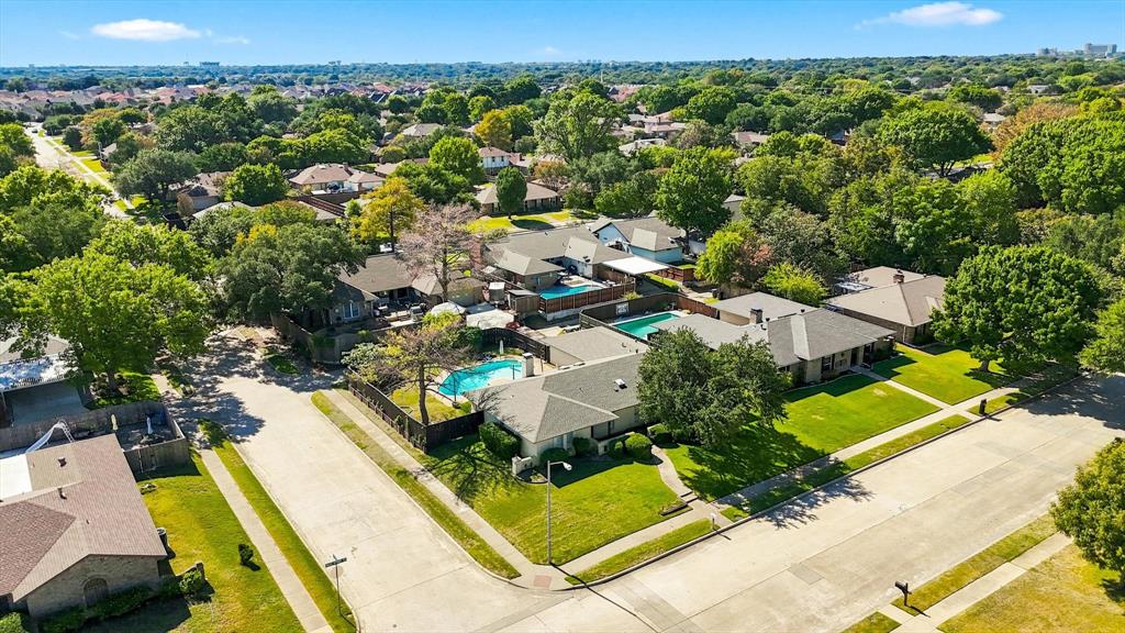 Aerial perspective of a corner lot property featuring a residential structure, a private swimming pool, mature perimeter landscaping, and asphalt street access