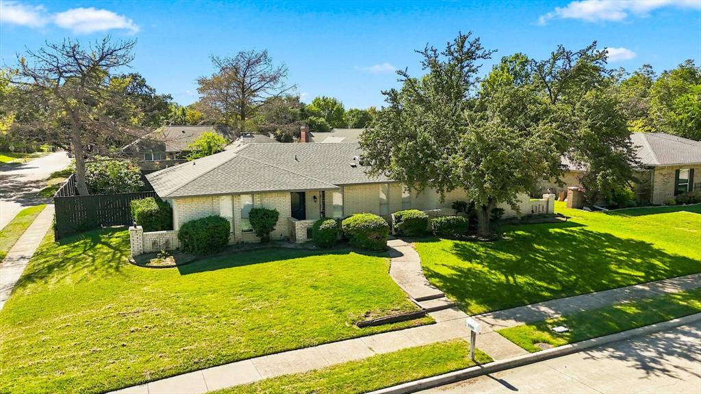 Single-story residence featuring a light-toned masonry exterior, a multi-gabled shingle roof, a concrete walkway, and an expansive lawn with mature trees