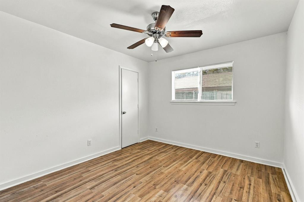Interior room featuring wood-finish flooring, a multi-blade ceiling fan with integrated lighting, and a single-panel interior door