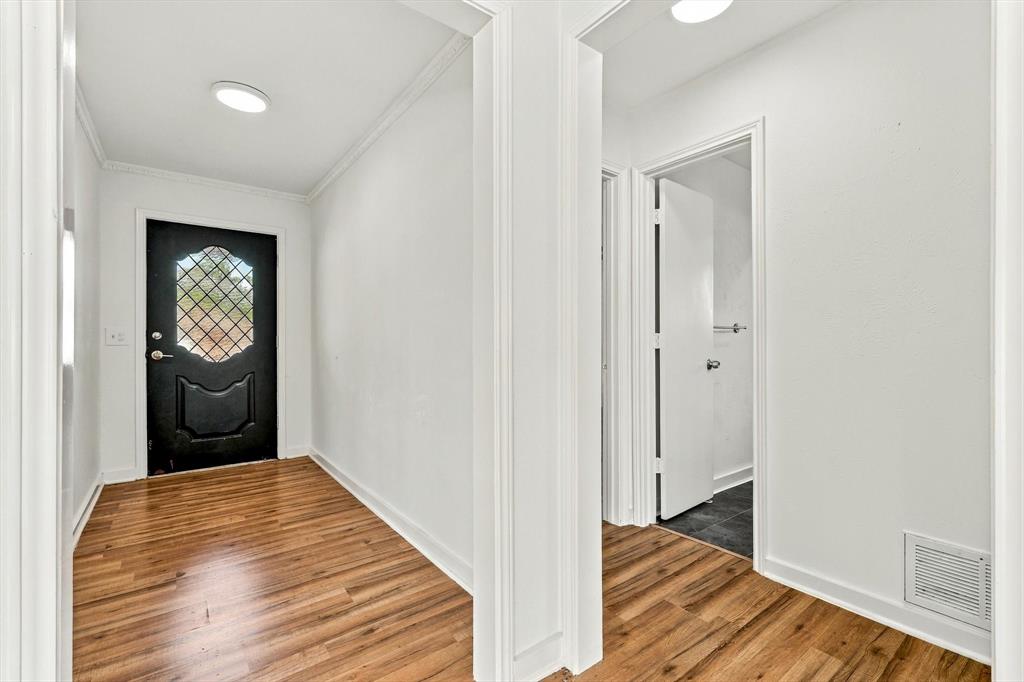 Entryway featuring wood-finish flooring, white walls, crown molding, and a solid black exterior door with decorative lattice-patterned glass