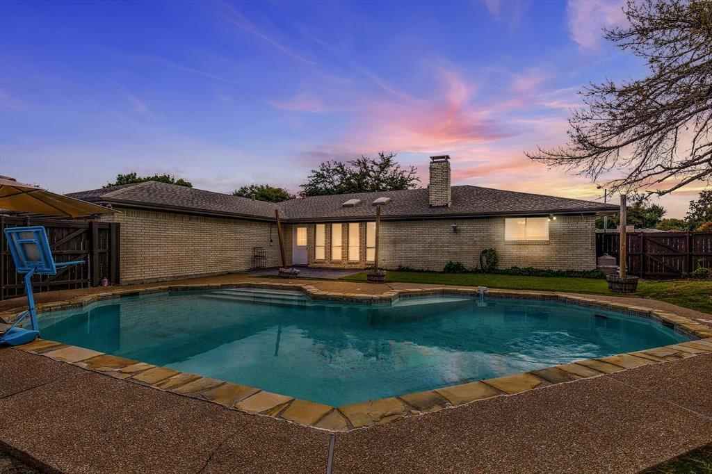 Exterior featuring a brick facade, chimney, in-ground swimming pool with stone coping, and fenced perimeter